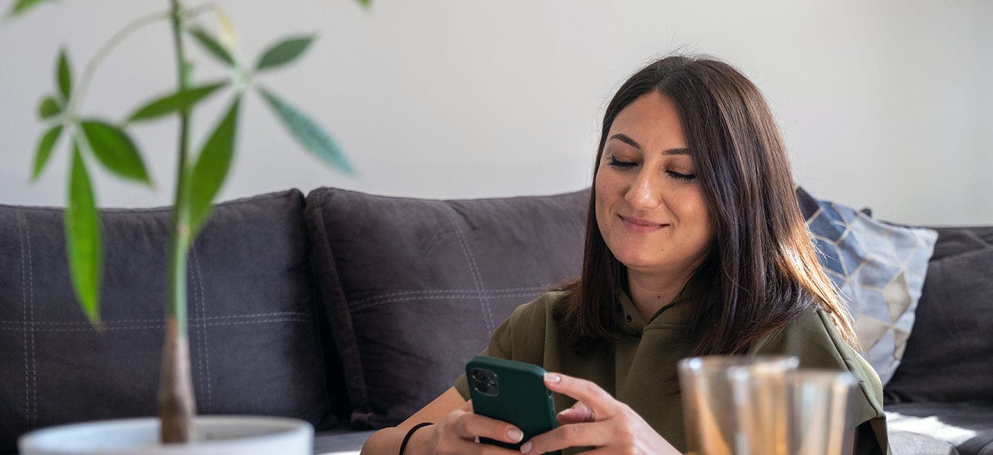A picture of a young woman using her smart phone at home.
