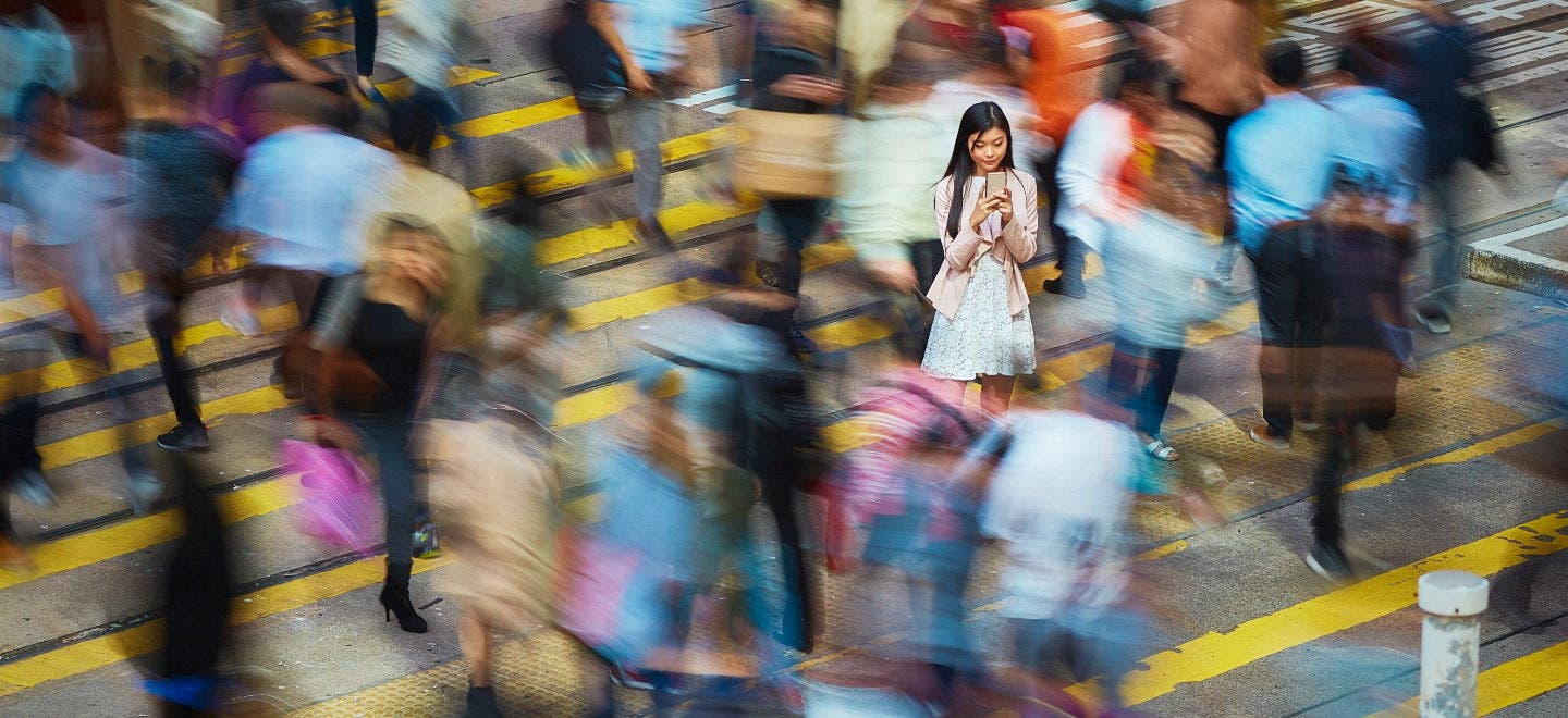 High angle view of young professional using mobile phone amidst crowd. Businesswoman is standing on busy street. She is surrounded by people in city.